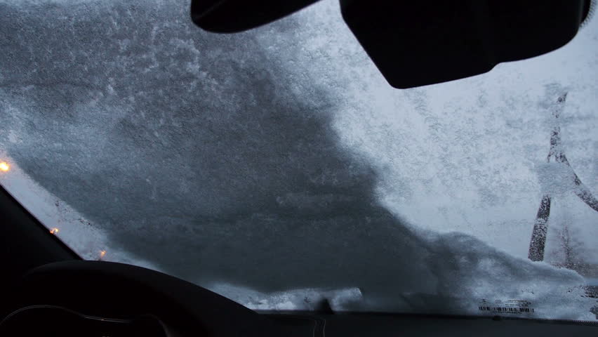 A man cleans off the snow and ice from his windshield.