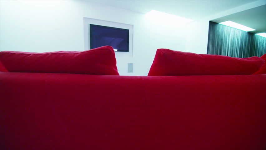 Excited group of friends rush to take a seat in luxurious contemporary home television viewing area with curved red sofa and wall mounted screen