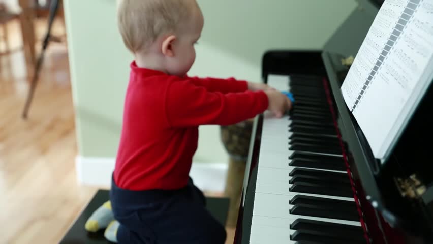 A toddler boy playing on a black upright piano in his home