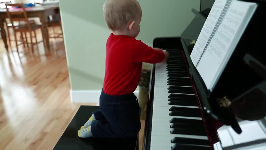 A toddler boy playing on a black upright piano in his home
