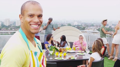 Portrait of a happy young man cooking barbecue for his friends on a penthouse terrace with views of the city.