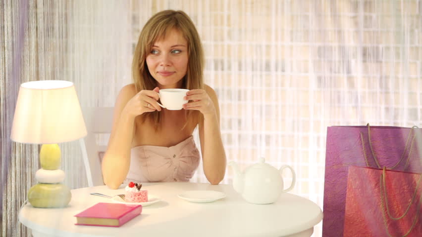 Charming girl sitting at cafe drinking tea looking at camera and smiling