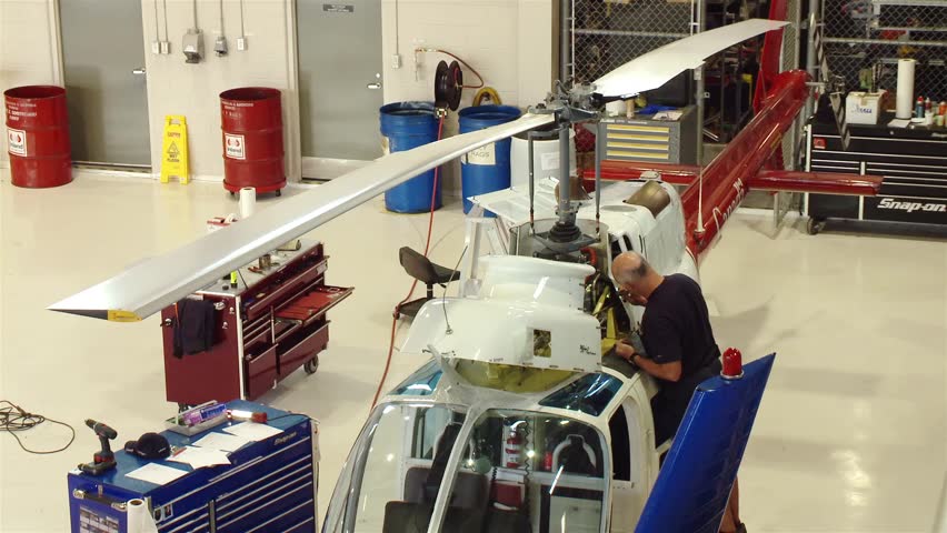 A man works on a helicopter in a hangar.