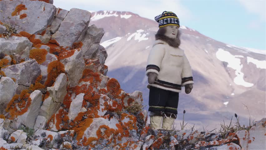 Handmade inuit doll displayed on rocks near a mountain in Arctic Bay, Nunavut.