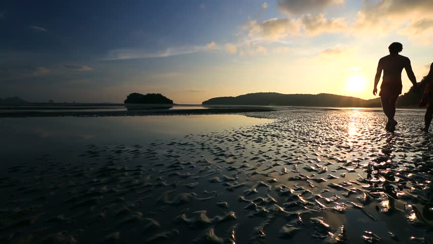 Young couple walking on a beach at sunset in Krabi, Thailand. Low tide.