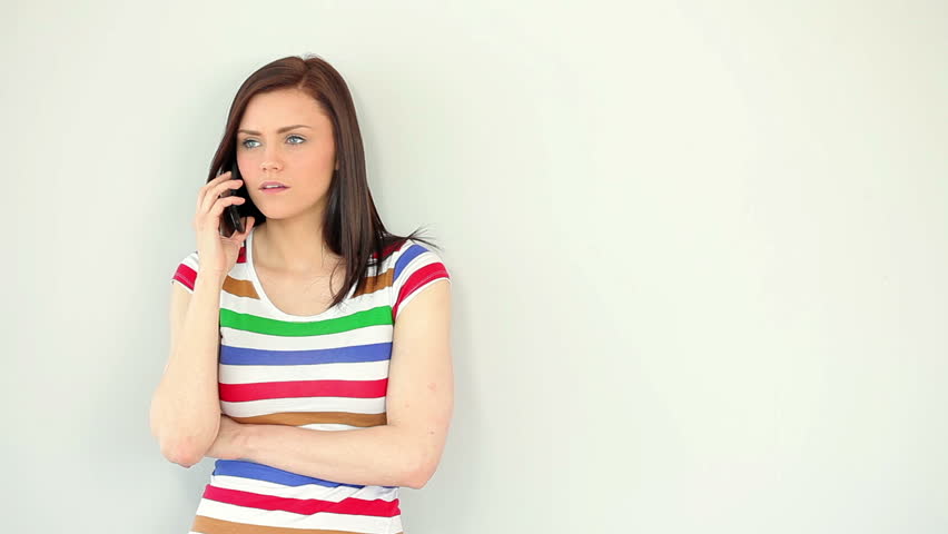 Annoyed young woman talking on her phone against a white wall