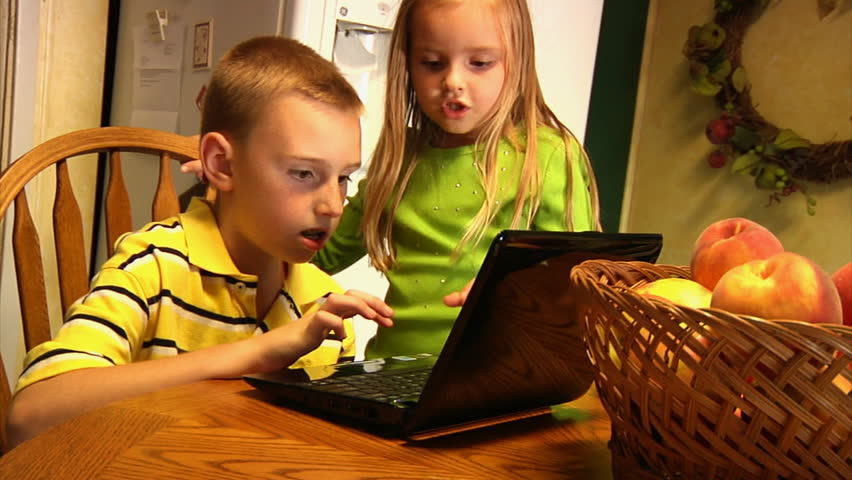 Young children use a laptop in the kitchen.