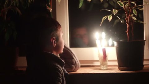 A boy looks out the window at night, lit candle on a windowsill
dramatization of a global cataclysm, turn off the electricity. Picture intentionally made ??as dark.
