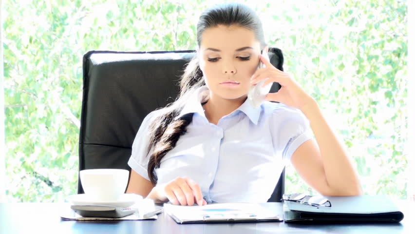 Angry young businesswoman using mobile phone and drinking coffee 