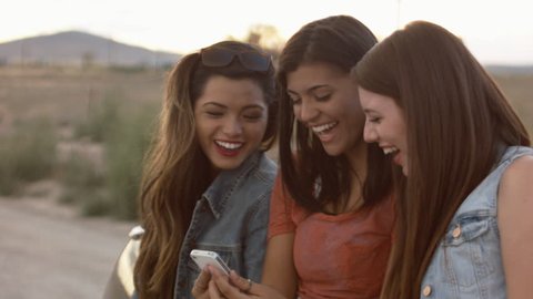 Multi Ethnic Group Of Teen Girls Laughing At A Phone Together In The Desert