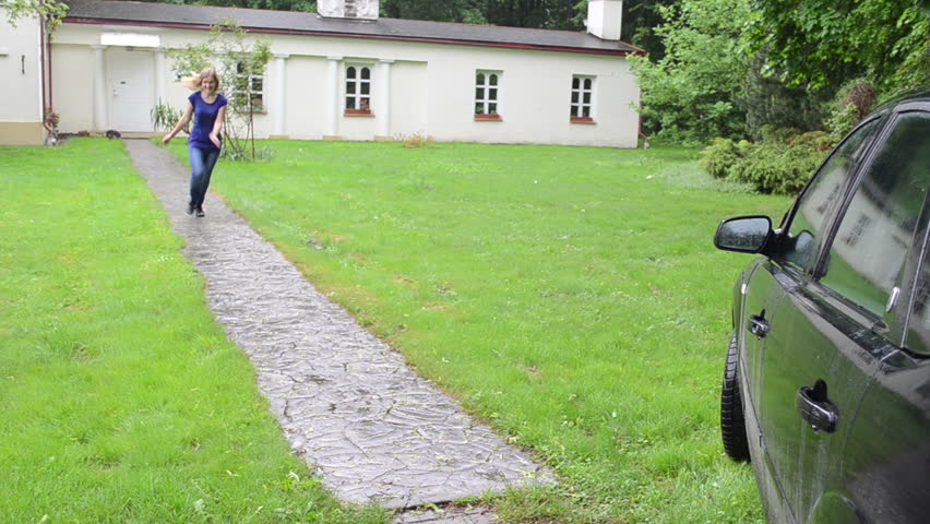 Hasten blond female driver woman run toward car automobile through cobbled path in strong rain.