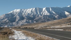 Winter traffic mountain road beautiful scenery 4K. Rural valley road with traffic cars. Majestic snow covered mountain towers. Farm and ranch land. Cold seasonal weather. HD 4K 1080 video.