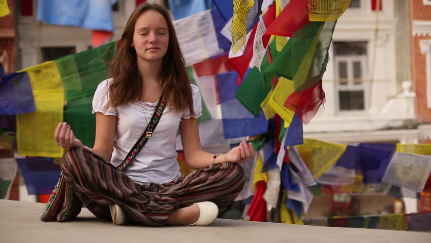 Teengirl meditating in Lotos pose on the background of fluttering prayer flags.