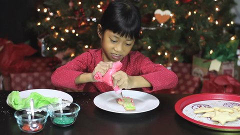 A cute little seven year old Asian girl enjoys making beautiful Christmas cookies in time for the holiday season.