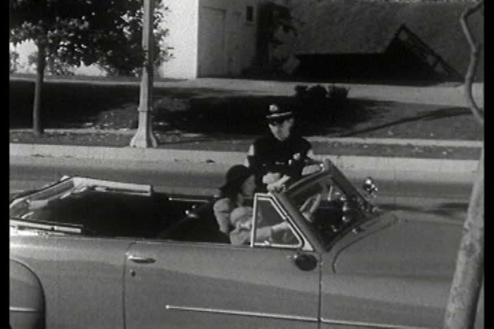 A police officer gives a woman a ticket for committing a traffic violation during the 1940s | Shutterstock HD Video #5318990