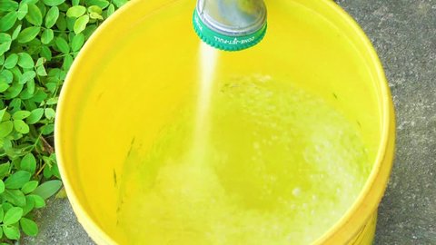Yellow plastic bucket being filled with water by a garden hose