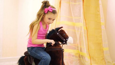 Girl in jeans and t-shirt swinging on brown rocking horse in the playroom
