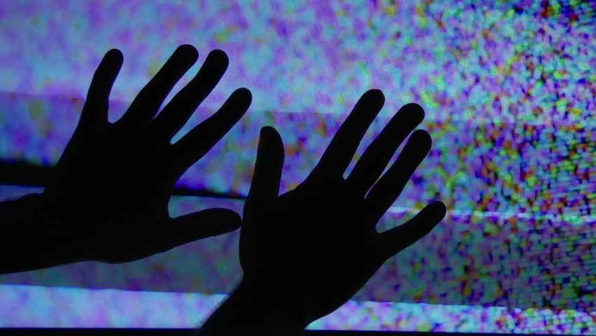 A mysterious set of hands touch the static on a television screen.