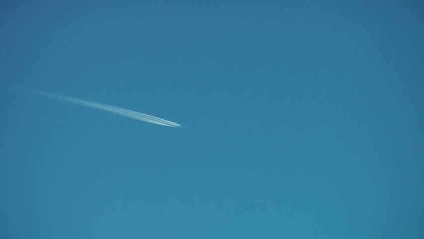 A Jet plane cuts across a perfectly clear blue sky, leaving a drifting vapor