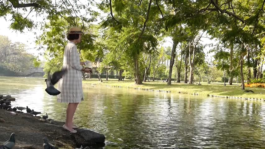 Asia woman feeding bird and fish in the  park pond.