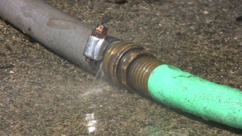 A leaking green and gray garden hose spills water onto the sidewalk.