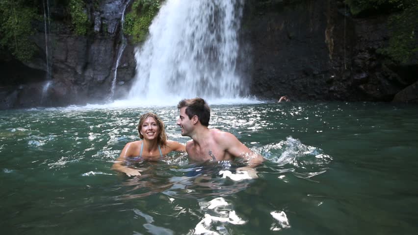 Couple swimming under waterfall