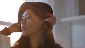 Close up clip, with natural sunlight flare, of a beautiful asian woman taking her newly bought hat from a shopping bag & trying it on.