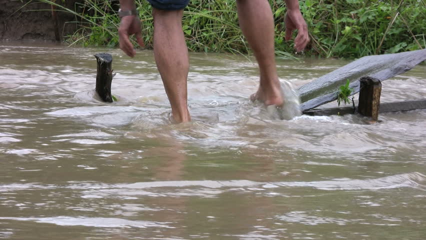 Two men work hard to repair a washed out bridge over a swollen creek in the middle of the rainy monsoon season in Thailand.