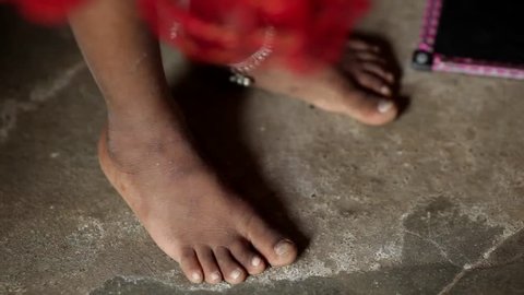 A closeup shot of a young Indian girl's feet moving and dancing against the stone floor. She wears an anklet and red dress.