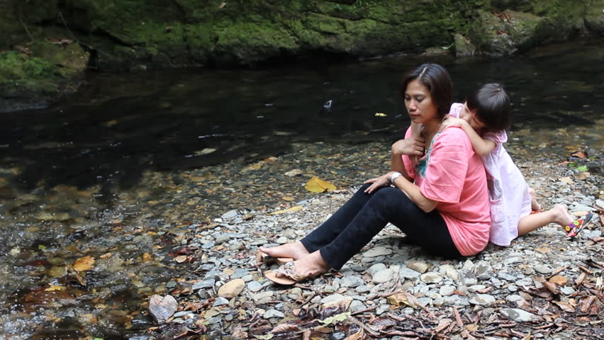 little girl and mother by a river embracing 