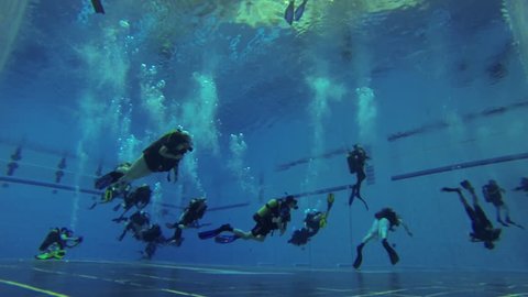 Group of scuba divers swimming past in a pool, learning to dive
