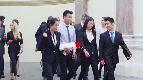 Confident Asian business team chat as they walk through busy conference building