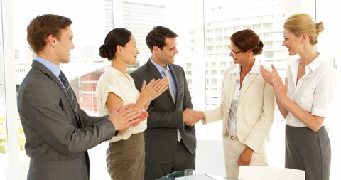 Business people shaking hands at interview while others clap at the office