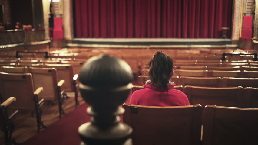 Hispanic woman alone in theater, seated waiting for show
