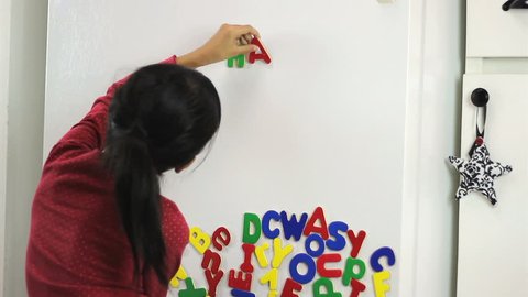 A cute little seven year old Asian girl uses colorful fridge magnet letters to spell Happy Birthday!