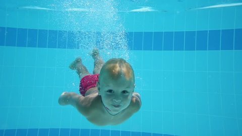 Cute little boy dives in blue pool with open eyes and floated back