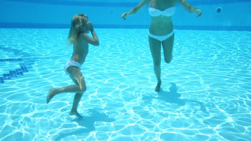 Mother with daughter in swimsuits swim under water in the pool