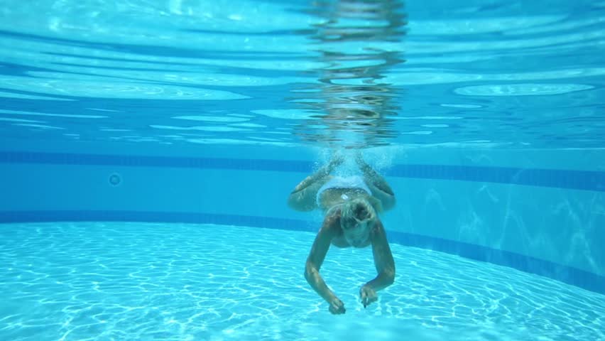 Beautiful girl in swimsuit swim under water in pool and make ok gesture