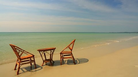 Wild beach.Two empty wooden chairs and table standing in a water.