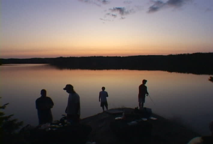 People enjoy beautiful sunset at campsite near calm lake water in Minnesota.