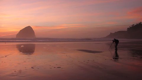 Colorful sunset at Pacific Ocean, Oregon Coast with photographer shooting still camera on tripod.