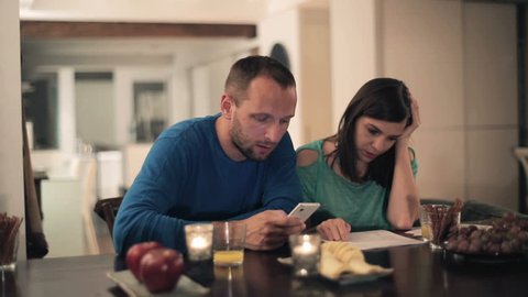 Sad, overwhelmed couple counting bills by the table at home
