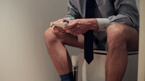 Businessman with smartphone sitting on toilet
