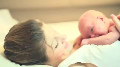 Mother and her Newborn Baby. Happy Mother and Baby kissing and hugging. Resting in bed together. Maternity concept. Parenthood. Motherhood   Beautiful Happy Family Stock Video Footage. Slow Motion