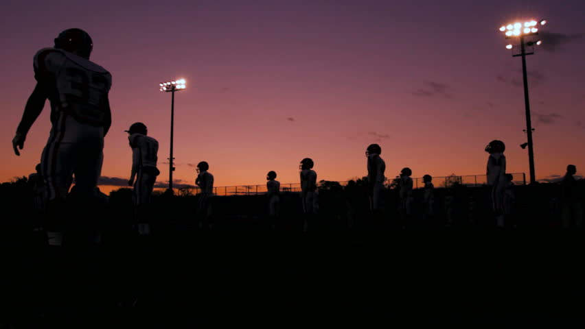 Shilouetted football players doing jumping jacks as a team as the sun sets.