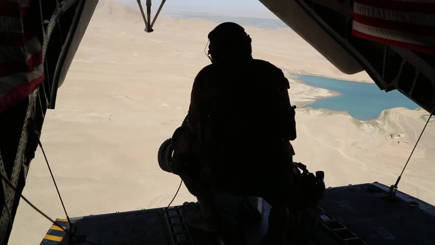 Tail Gunner Sits in Open Doorway of Helicopter over Afghanistan  while U.S. Flags Wave in the Breeze