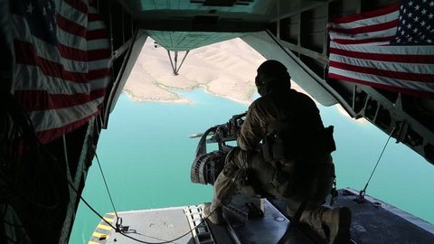 Tailgunner Sits in Open Doorway of Helicopter over Afghanistan while U.S. Flags Wave in the Breeze