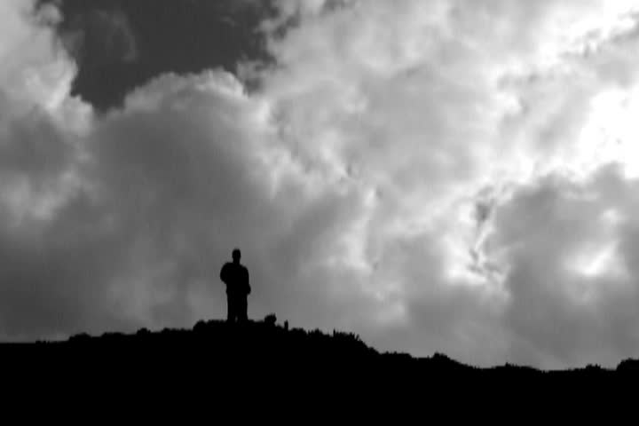 Man stands high up on summit with composite of clouds time lapse. 