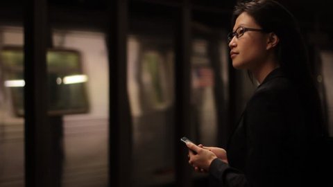 As a train passes, a woman checks her mobile device on the dark subway platform. स्टॉक वीडियो