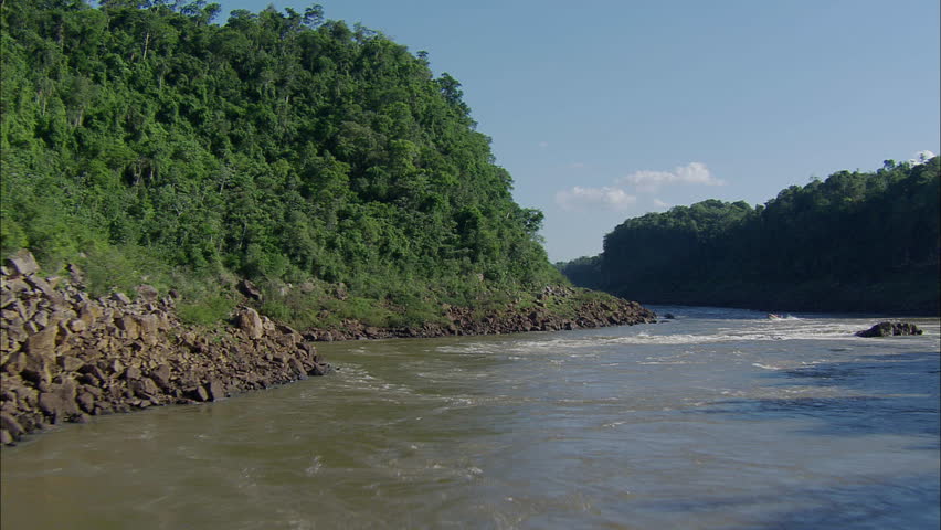 Waterfall River Paradise Rapids. The shot moves through a snaking river. An incredible view of inside the river canyon walls is shown. Rocky boulders and trees surround the falls.